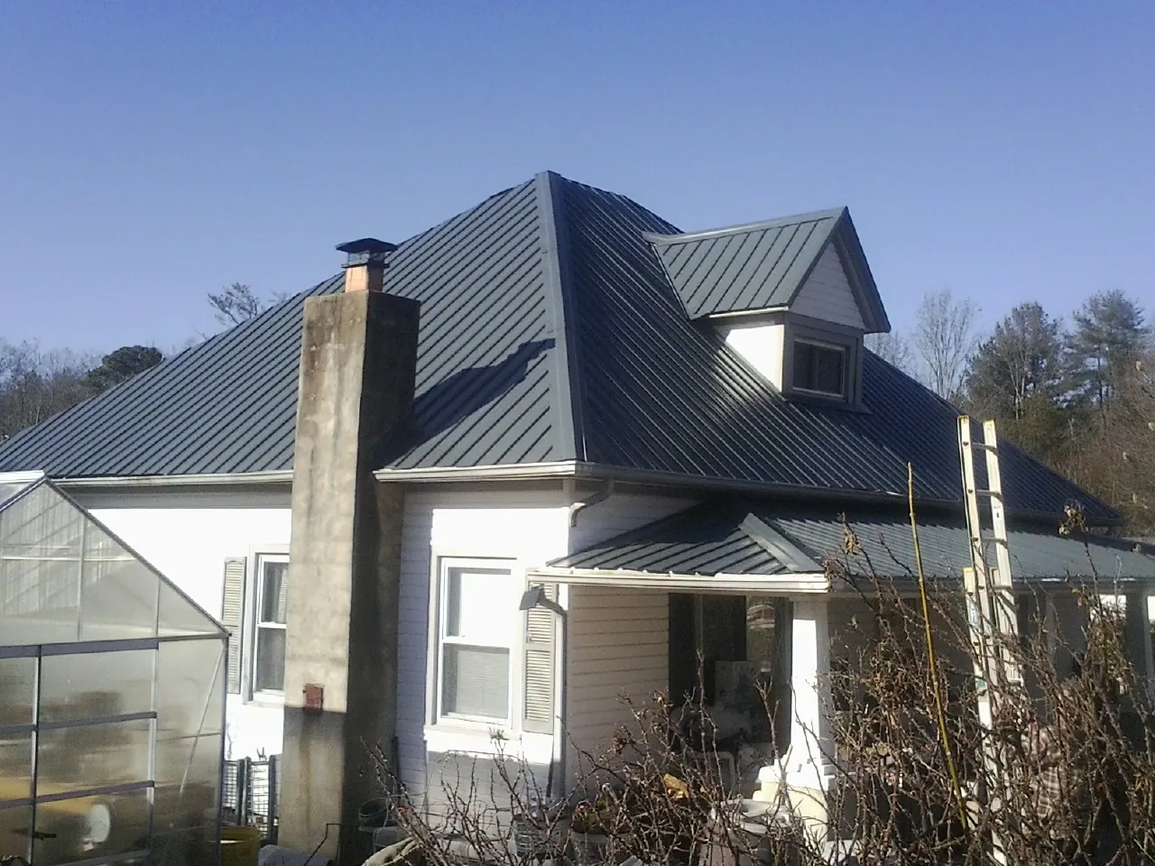 Dark blue standing seam metal roof on a white farmhouse with dormer — Slate & Tile Roof Repair by Roofing Brothers in Loraine