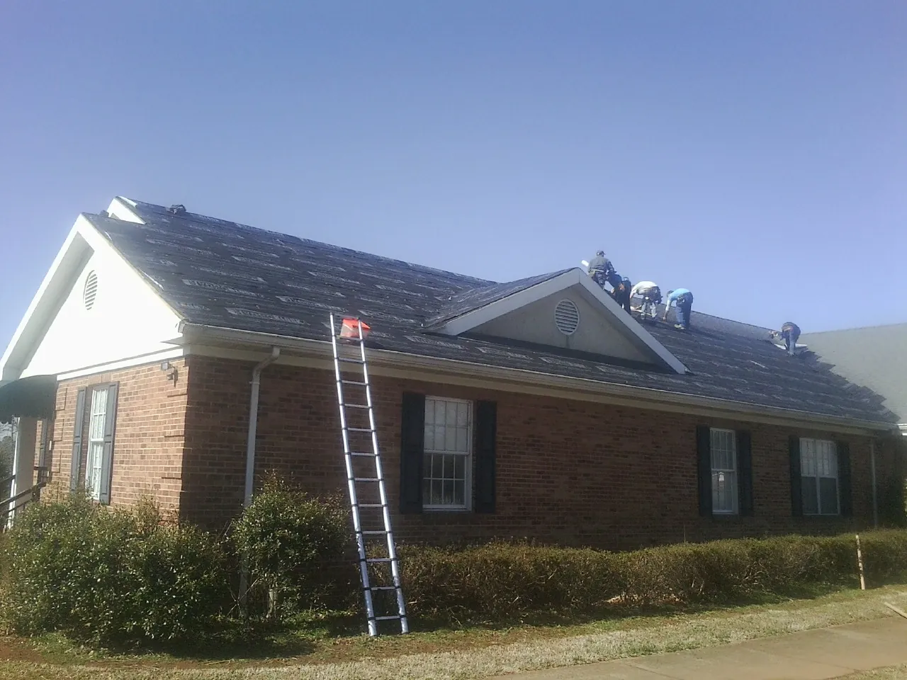 Crew tearing shingles off a brick ranch roof with a ladder set — Emergency Roof Repair work by our crew in Loraine