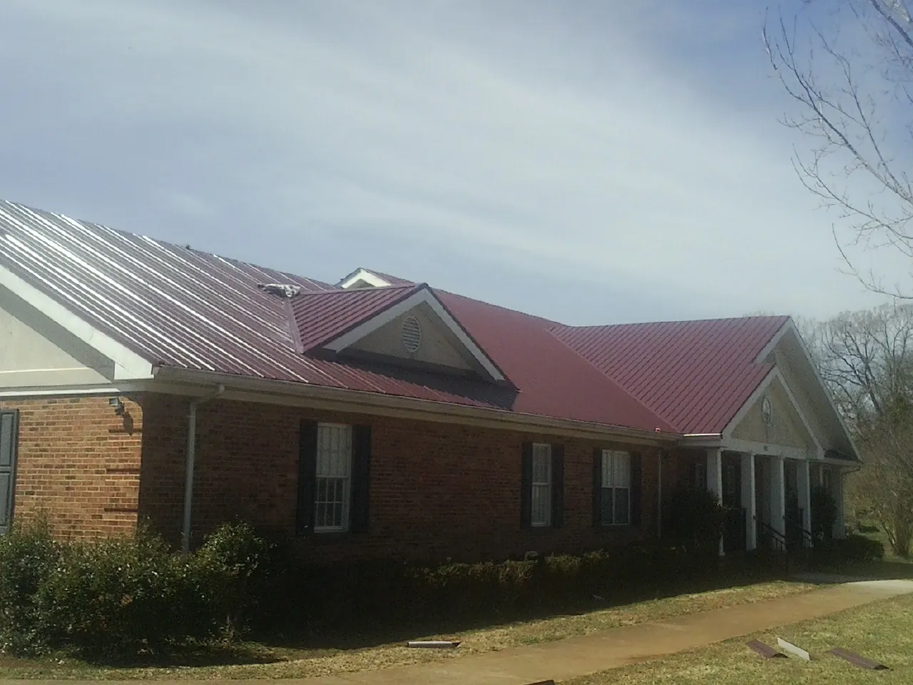 Red metal roof with gabled entries on a long brick building, from a Hail Damage Roof Repair job in Loraine