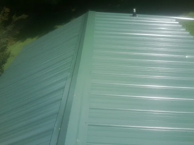 New green metal panels meeting at the ridge of a roof — Flat Roof Repair work by our crew in Loraine