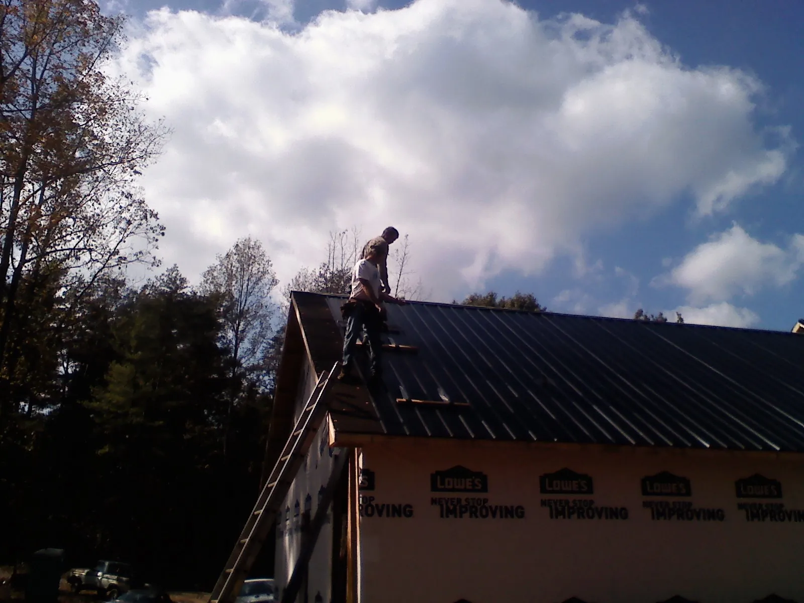 Roofer fastening dark metal panels high against a cloudy sky, from a Roof Inspection job in Loraine
