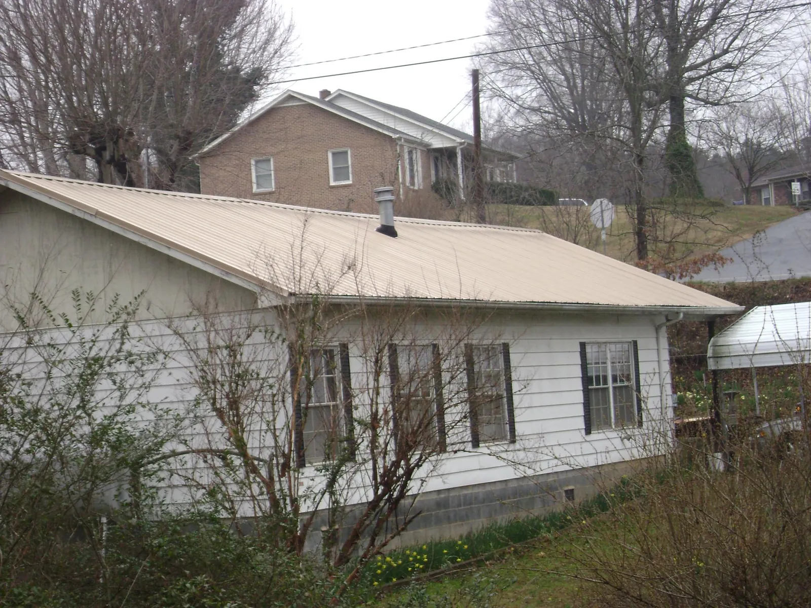 Tan metal roof on a white sided house set into a hillside — Commercial Roofing by Roofing Brothers in Loraine
