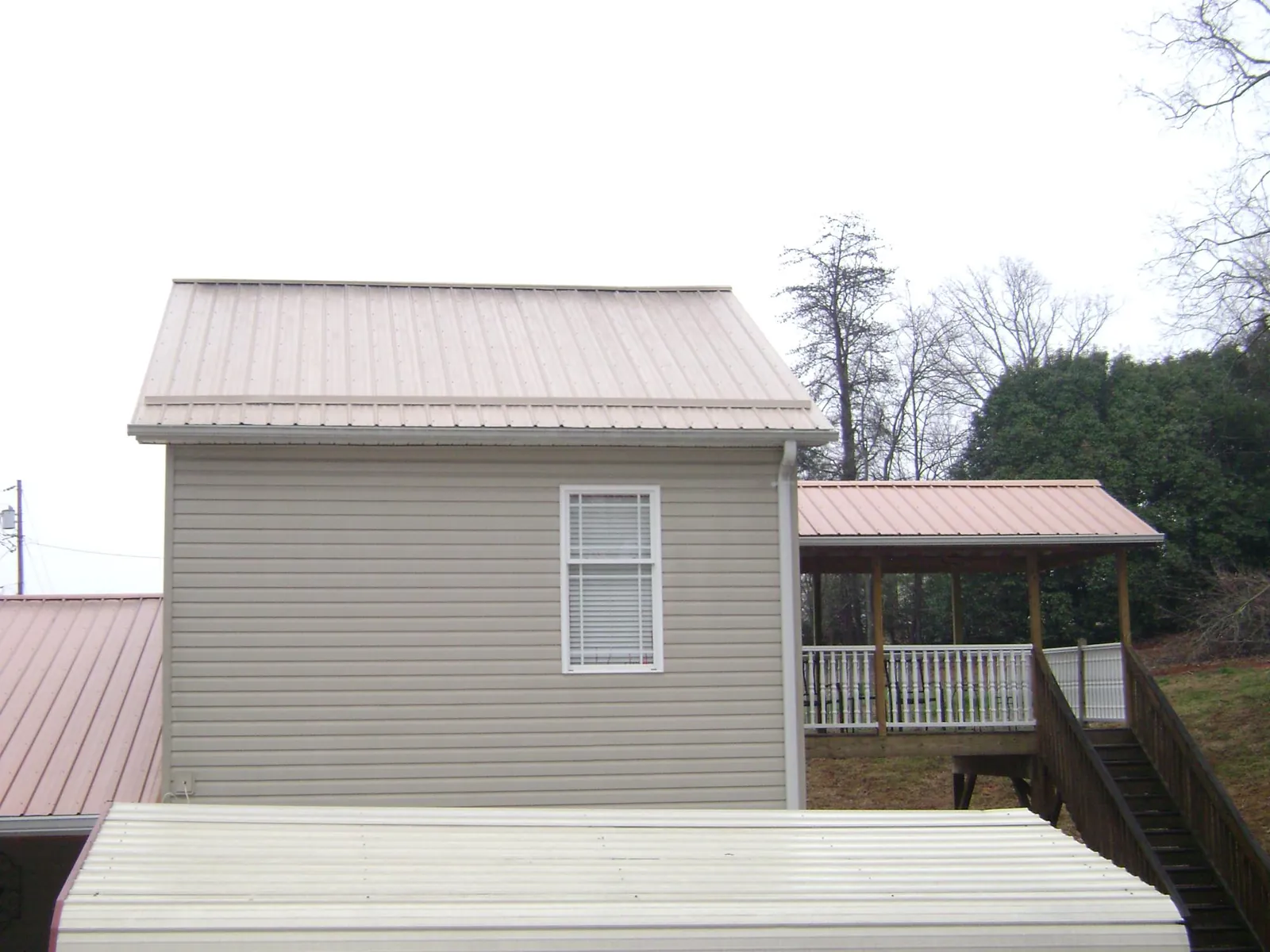 Tan metal roofs on a two story addition and attached porch, from a Roof Replacement job in Loraine